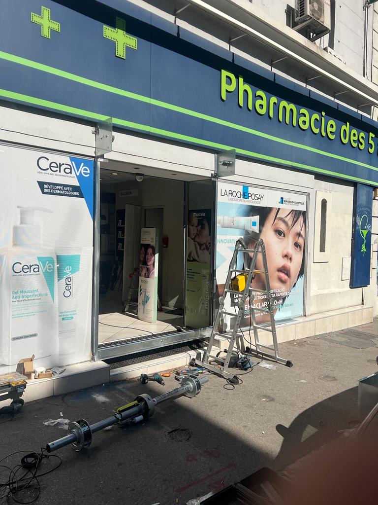 Axe d’enroulement et moteur déposés sur le trottoir pendant le remplacement du rideau métallique d’une pharmacie