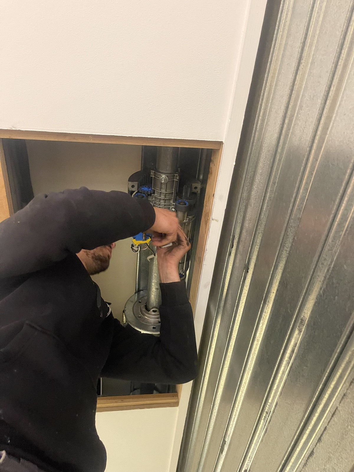 Technicien réglant le moteur d’un rideau métallique par la trappe de visite